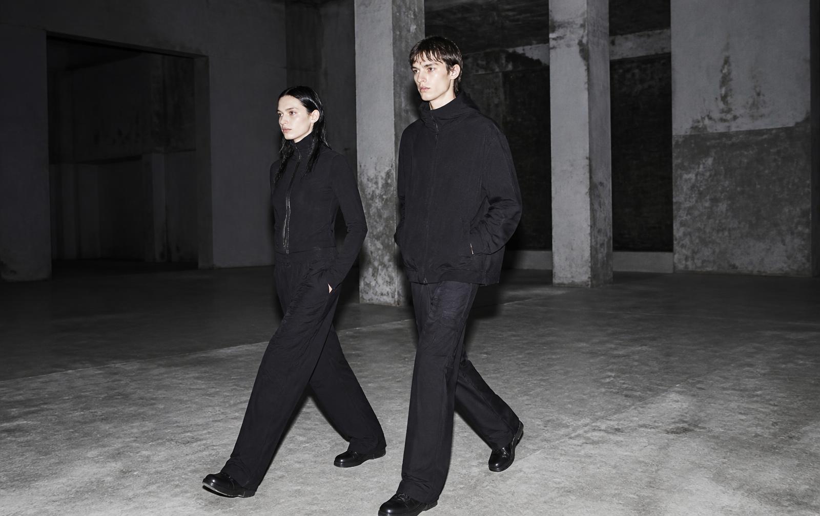 Two models walking through an empty industrial hall in all-black athleisure
